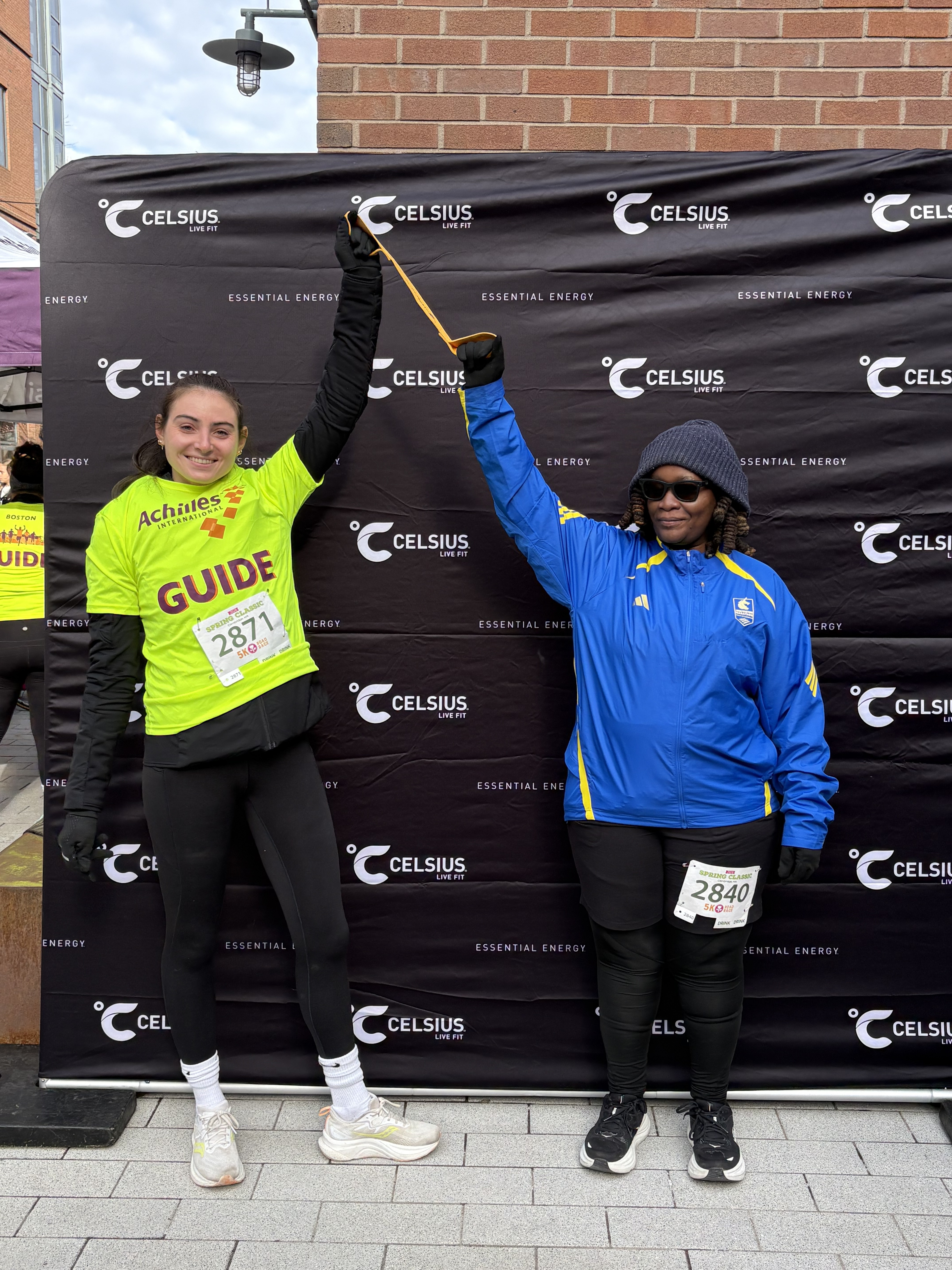 Two women connected by a tether for visually impaired runners at the finish line.